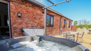 Un jacuzzi situé devant un bâtiment en briques, avec un patio et du mobilier d’extérieur.
