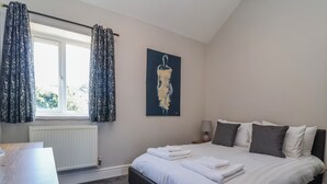 Une chambre à coucher avec un lit, un radiateur, une fenêtre avec des rideaux, un tableau et une table de chevet.
