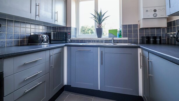 Une cuisine moderne avec des meubles gris, un four à micro-ondes encastré et une fenêtre donnant sur un paysage verdoyant.