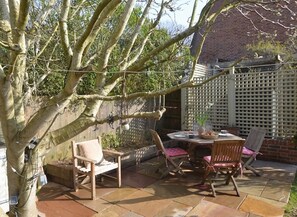 Une terrasse avec une table et des chaises, un banc en bois et un arbre.