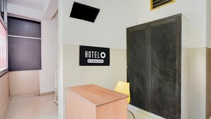A hotel reception area with a wooden desk, a yellow chair, a large dark-framed door, and a sign that reads 'HOTELO Company Serviced.' - Deluxe BV Stayz (Chennai)