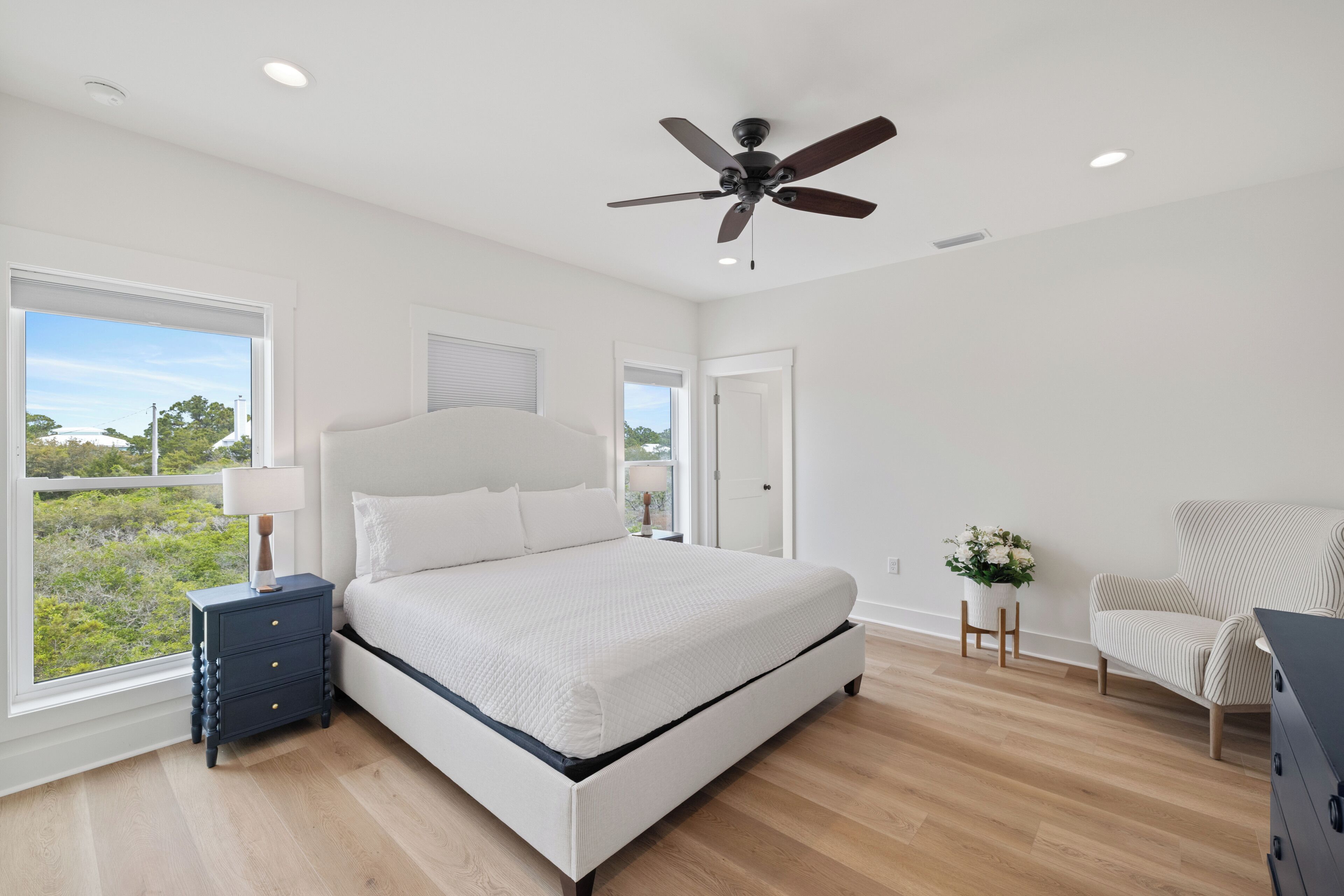 A bedroom with a bed, a ceiling fan, a nightstand, a chair, and a window with a view.