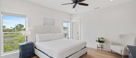 A bedroom with a bed, a ceiling fan, a nightstand, a chair, and a window with a view.