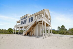 Ein Strandhaus mit einer Holztreppe, die zu einem Balkon führt.