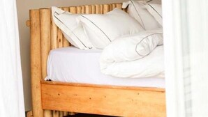 A wooden bed with white bedding, a plain wall, and three framed pictures above it.