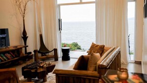 A living room with a sofa, a TV, a bookshelf, and a view of the sea.