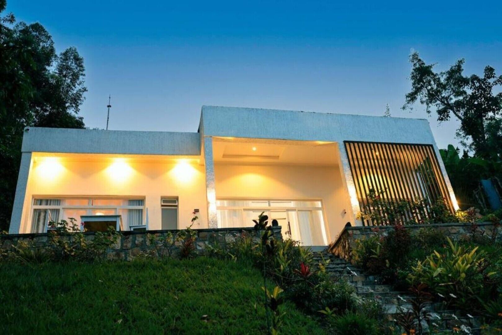 A modern two-story house with a stone wall in front, a large window on the ground floor, and a sloped roof.