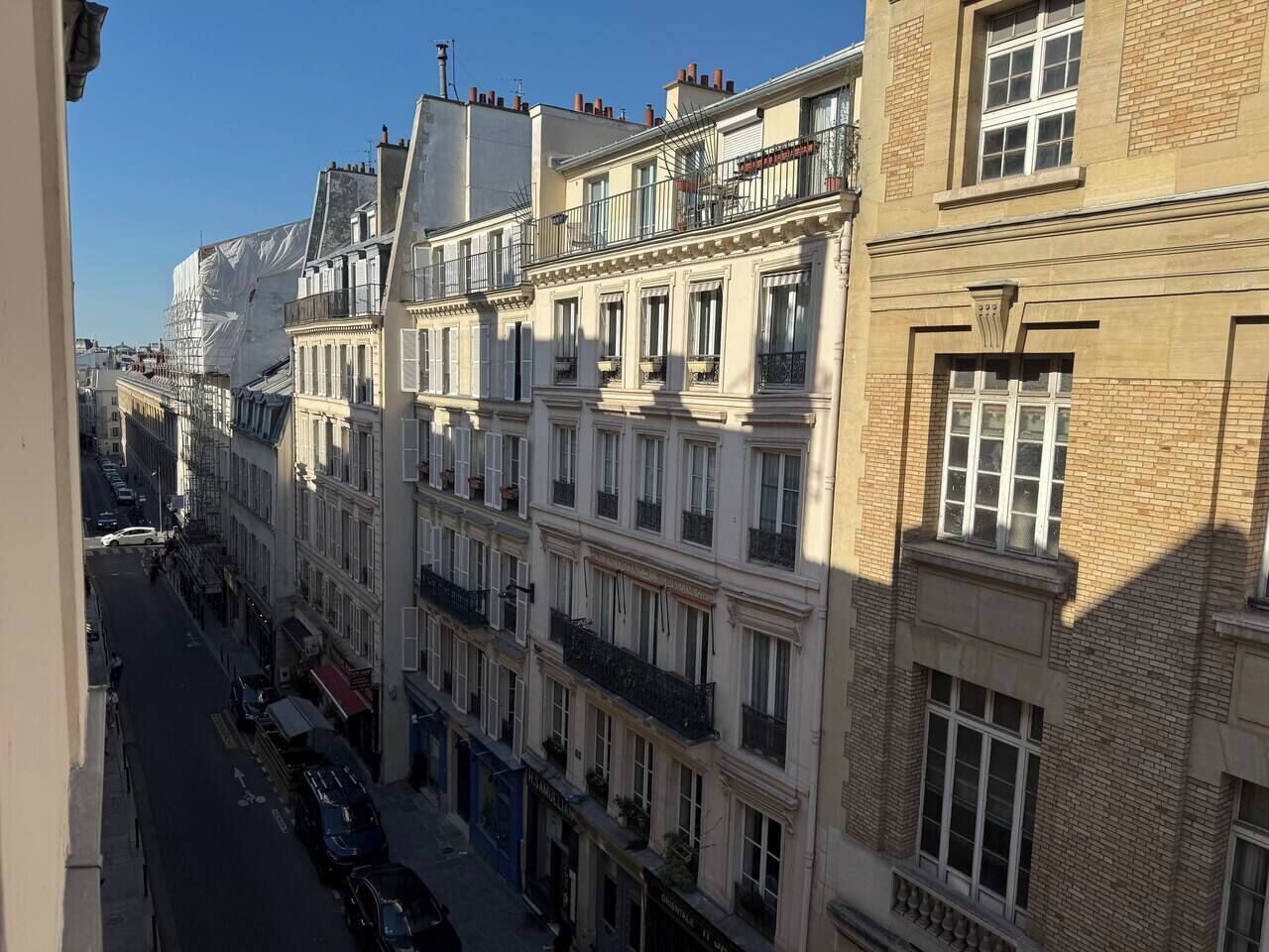 A row of multi-story buildings with balconies, a street in the foreground, and a clear sky.