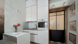 Cocina compacta con armarios blancos, horno integrado y un pequeño comedor con banco.
