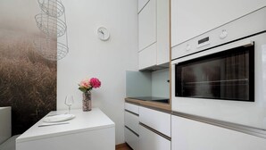 Una cocina moderna con armarios blancos, horno integrado, un reloj y un florero con flores en la encimera.