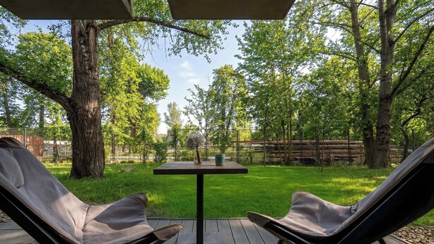 Una terraza al aire libre con dos sillones de descanso, una mesita y vistas a un jardín con árboles.