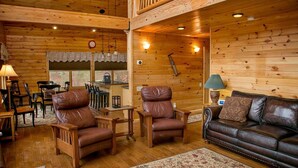 Ein gemütliches Blockhaus mit Holzwänden, einem Ledersofa und einem Essbereich mit Stühlen und einem Tisch.