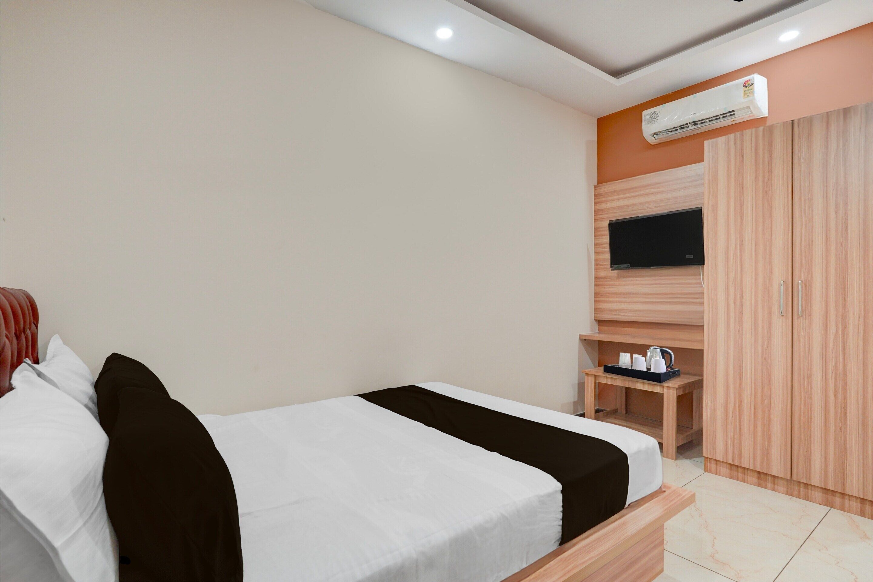 A hotel room with a bed, a TV mounted on the wall, a wardrobe, and a small table with a tray.