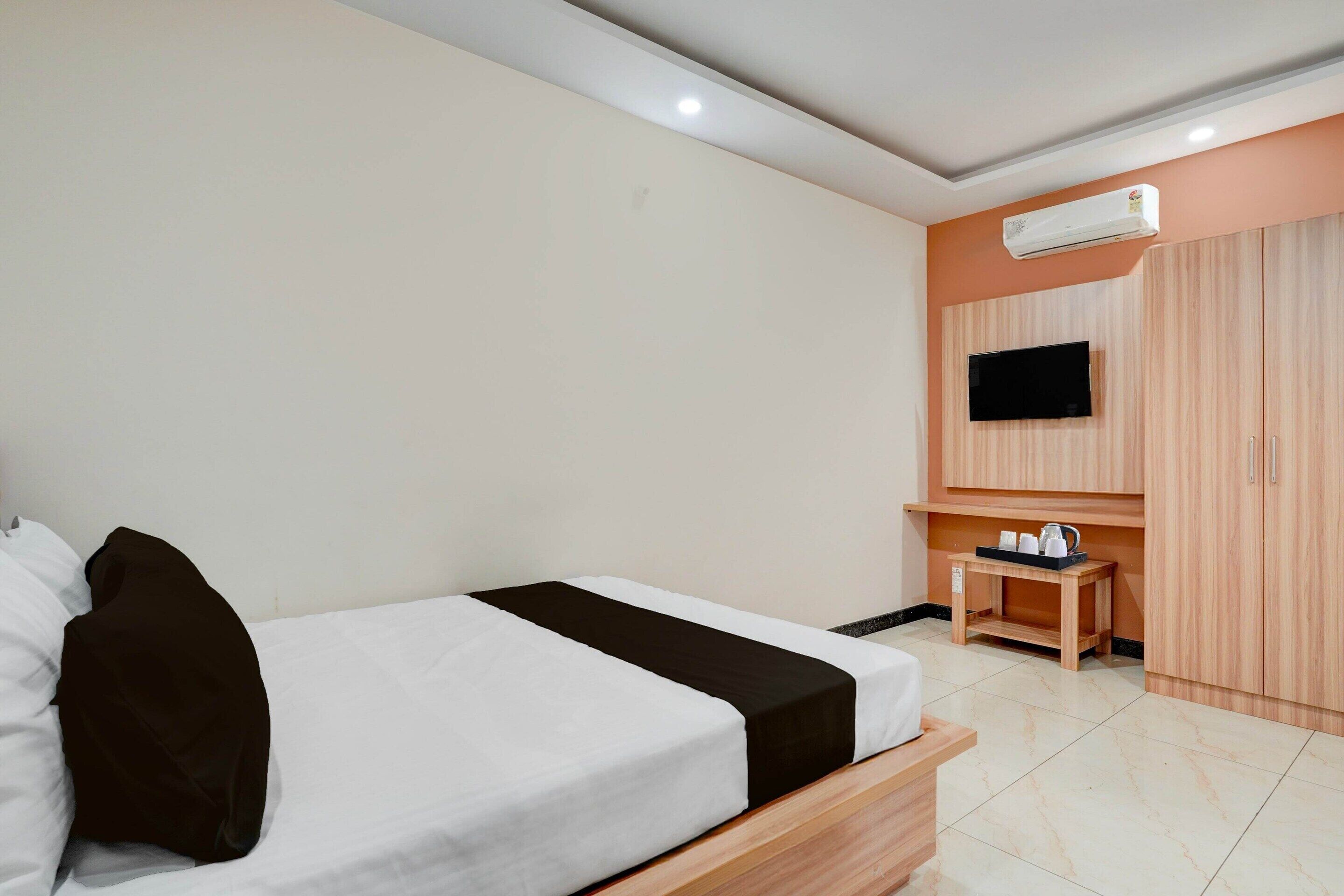 Een hotelkamer met een bed, een aan de muur bevestigde televisie, een houten garderobe en een klein tafeltje met een dienblad.