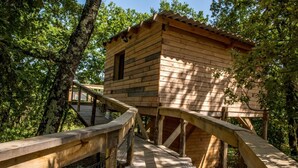 Eine Holzhütte mit einer Holzterrasse und einem Metallgeländer, umgeben von Bäumen.