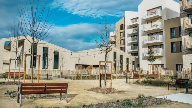 Un edificio residencial con varios balcones, un patio con bancos y cielo despejado.