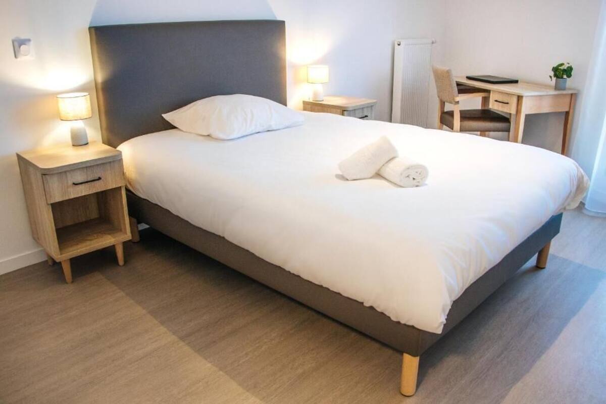 A hotel room with a bed, bedside tables, a desk, and a chair.