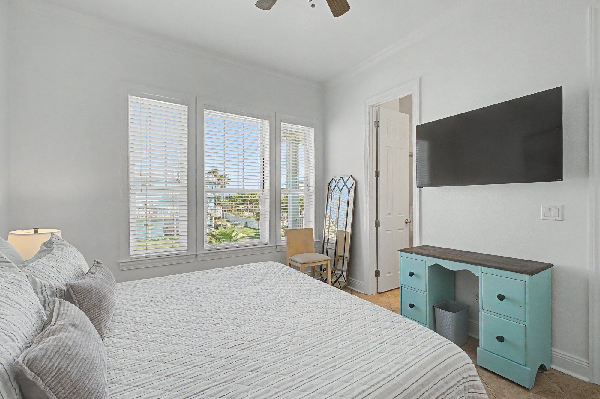 Een slaapkamer met een bed, een dressoir, een spiegel en een televisie aan de muur.