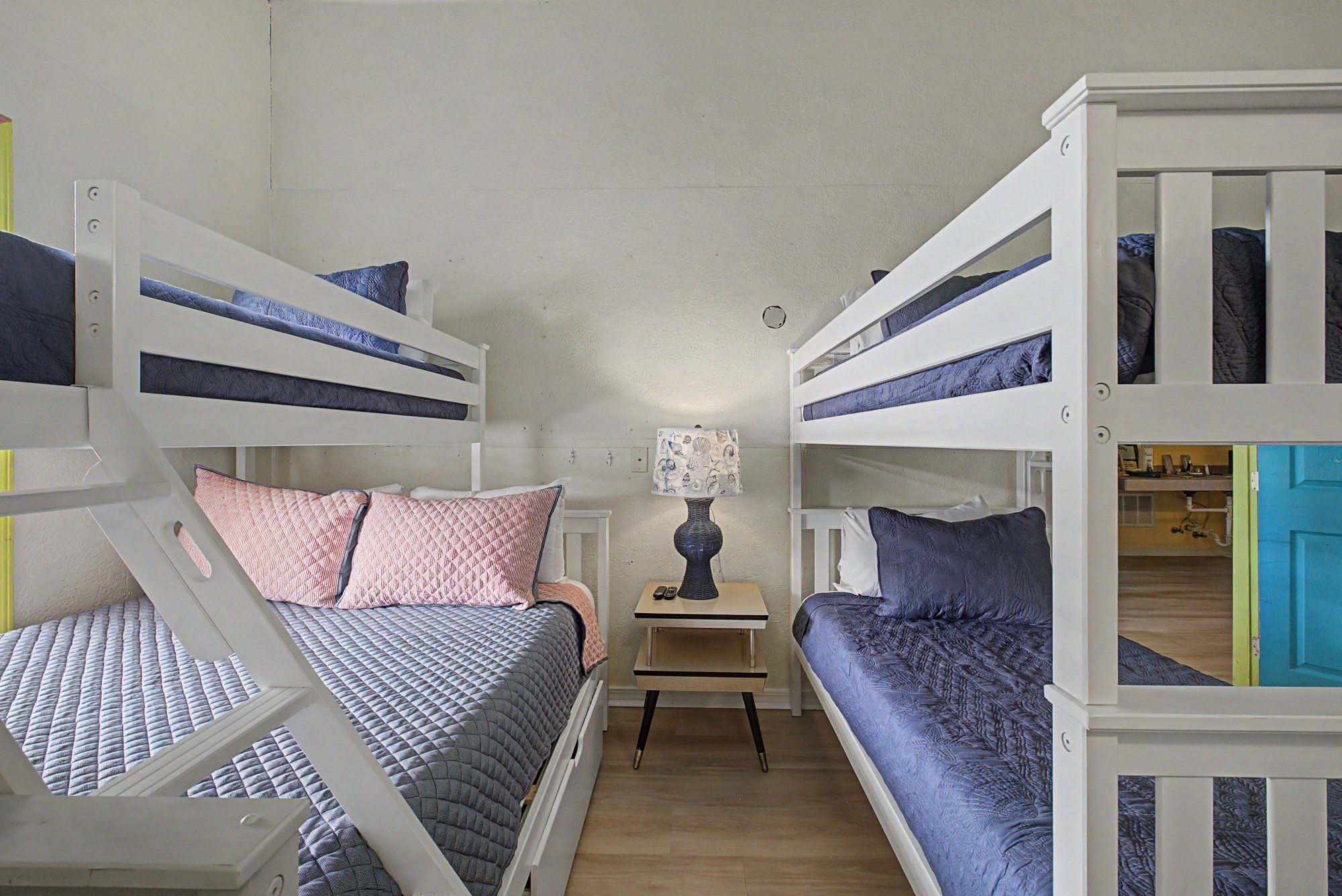 Una habitación con literas, una mesita de noche con lámpara y una puerta a otra habitación.