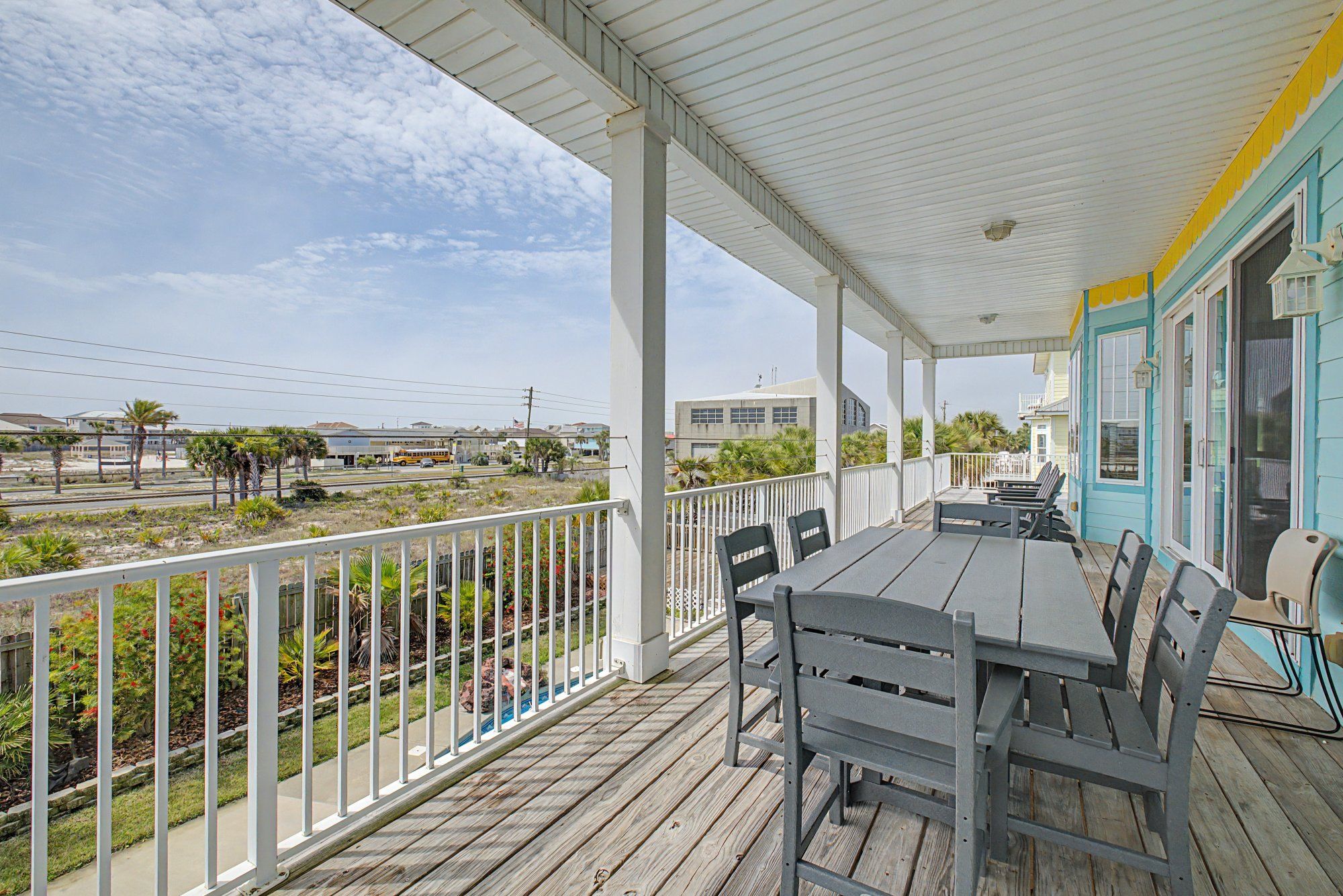 A covered outdoor area with a table and chairs, a white railing, and a view of the surrounding landscape.