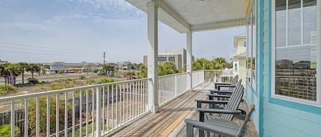 A covered outdoor area with wooden benches and a railing, overlooking a street and buildings.
