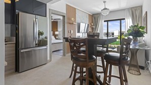A modern kitchen with a stainless steel refrigerator, wooden bar stools, and a dining table. - NOK Modern 2BR With Rooftop Jacuzzi By Vistacana (Punta Cana)