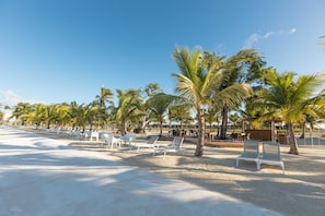 A beach with white lounge chairs and palm trees. - NOK Modern 2BR With Rooftop Jacuzzi By Vistacana (Punta Cana)