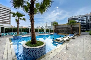 Ein Pool auf dem Dach mit gefliesten Rändern, Palmen und Liegestühlen.
