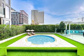Ein Pool auf dem Dach mit kreisförmigem Design, umgeben von ordentlich gestutztem Rasen und einer Glasbrüstung.