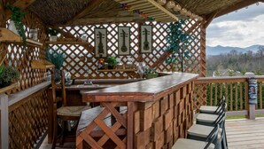 A wooden deck with a bar area, seating, and a view of mountains. - Poolside ADU w Sauna Free Tix Tiki Bar Retreat (Candler)