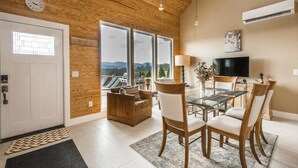 A modern living room with a wooden ceiling, a dining area with glass tables, and a large window with a mountain view. - Poolside ADU w Sauna Free Tix Tiki Bar Retreat (Candler)