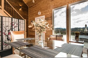 Interior moderno com mesa de jantar de vidro, paredes de madeira, vista para o exterior e um ecrã tradicional japonês.