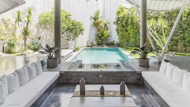 Ein Poolbereich mit modernem Design, der einen Pool, weiße gepolsterte Sitzgelegenheiten und Kübelpflanzen umfasst.