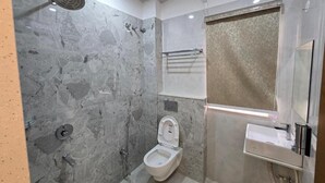 A bathroom with a marble wall, a toilet, a shower, and a sink. - Vaikuntha Stays Hotel (Indore)