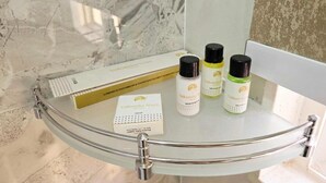 A bathroom with a glass shower enclosure, a white marble wall, and three bottles of Valkantha products on the sink. - Vaikuntha Stays Hotel (Indore)