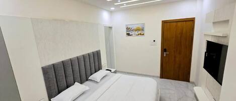 A modern hotel room with a bed, bedside table, TV, and a ceiling fan.