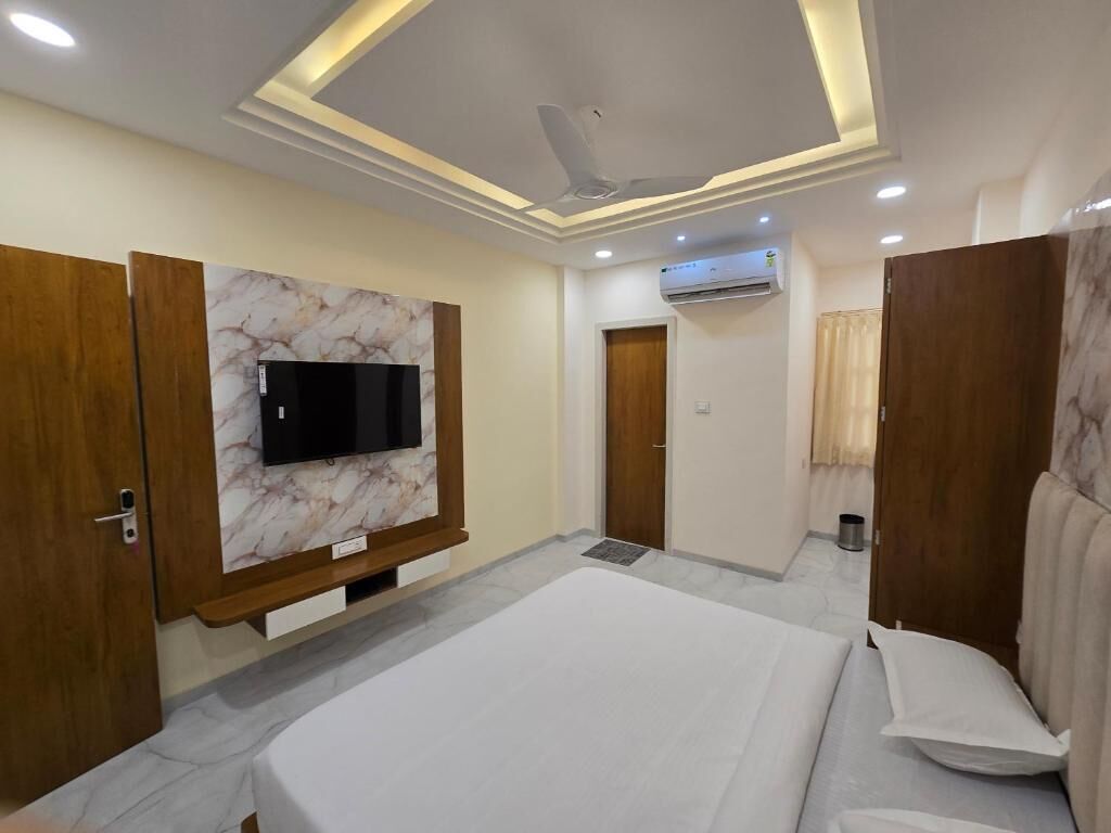 A hotel room with a bed, a TV mounted on a marble wall, a ceiling fan, and an air conditioning unit.