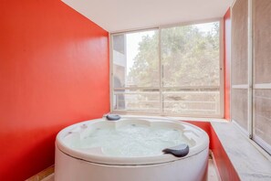 Une pièce avec un jacuzzi, une grande fenêtre et un mur rouge.