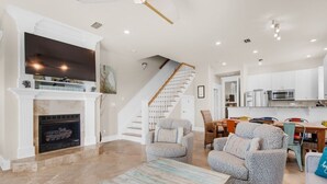 A spacious living room with a fireplace, comfortable seating, a staircase, and a kitchen area. - Your Front-Row Seat to Paradise, Pool, Balconies – Sleeps 14 (Miramar Beach)
