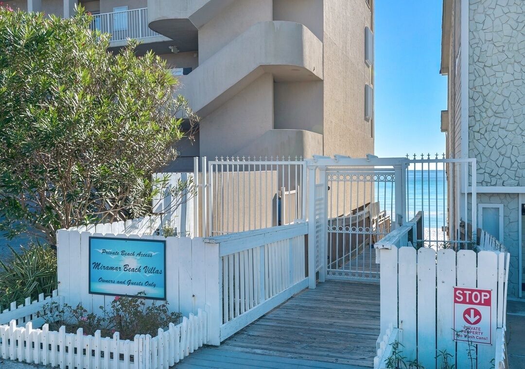 A gated entrance to a private beach area with a sign indicating 'Private Beach Access' and 'Miramar Beach Villas' for owners and guests only.