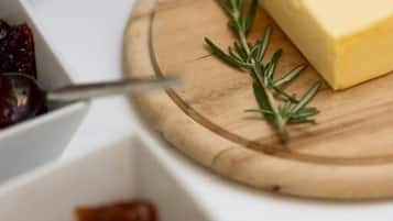 A wooden cutting board with a block of cheese and a sprig of rosemary.
