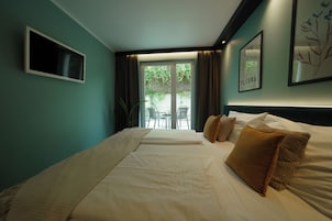Camera d'albergo con un letto, una televisione, un balcone con sedie e vista sul verde.