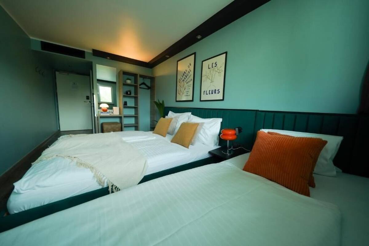 Een hotelkamer met twee bedden, een nachtkastje, een lamp en kunstwerken in een lijst aan de muur.