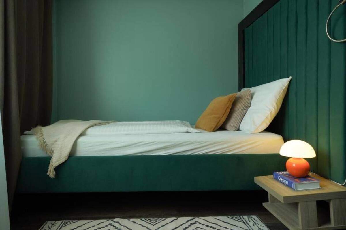 Een bed met een groen hoofdeinde, een bedlampje en een boek op een nachtkastje.