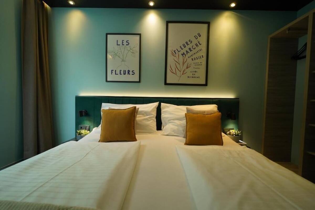 Een hotelkamer met een groot bed, twee kussens, een hoofdbord en twee ingelijste foto's aan de muur.
