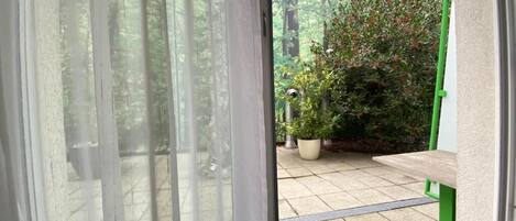 Un patio con un banco verde, plantas en macetas y vistas a través de un ventanal.