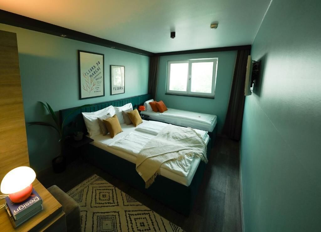 A bedroom with a bed, bedside table, lamp, framed pictures, and a window.