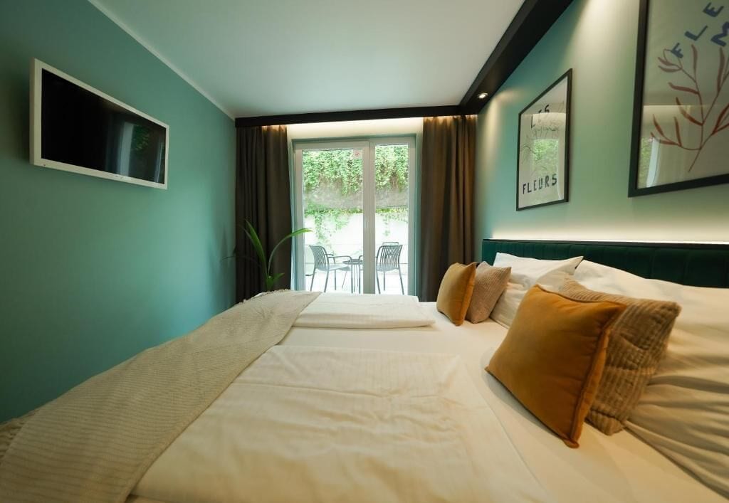 Una habitación de hotel con cama, televisión, ventana con cortinas y vistas a un espacio exterior.
