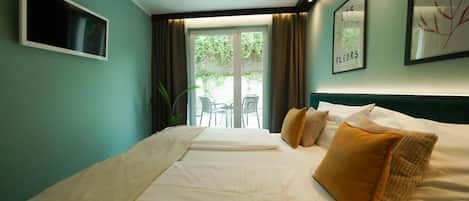 A hotel room with a bed, a TV, a window with curtains, and a view of an outdoor area.