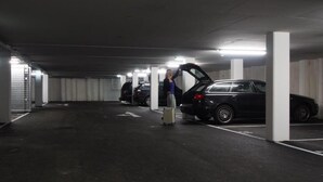 Eine Parkgarage mit mehreren Autos und einer Person, die neben einem Auto mit geöffneter Motorhaube steht.